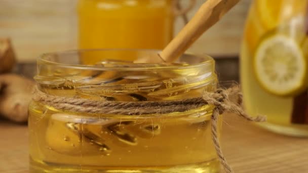 蜂蜜はスプーンのスピンドルからレモネードと生姜のジャグを背景に蜂蜜の瓶に流れます 免疫と健康をテーマにしたビデオ — ストック動画
