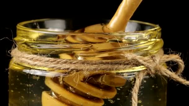 蜂蜜从勺子上流下来 倒入一个瓶中 瓶中的蜂蜜涂在黑色的背景上 — 图库视频影像