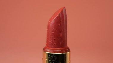 Red lipstick tube with water drops isolated on a pink background.