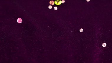 Multi-colored transparent jewelry crystals fall on burgundy velvet. Slow motion.