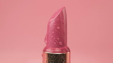 Red lipstick tube with water drops isolated on a pink background.