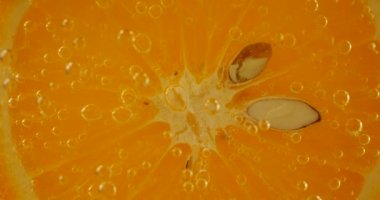 A slice of ripe orange in water bubbles on an orange background.