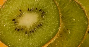 Ripe kiwi slices in air bubbles on an orange background.