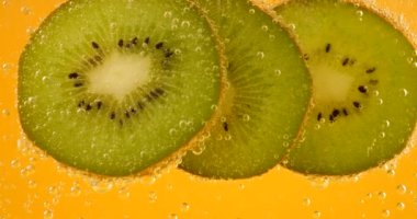 Ripe kiwi slices in air bubbles on an orange background.