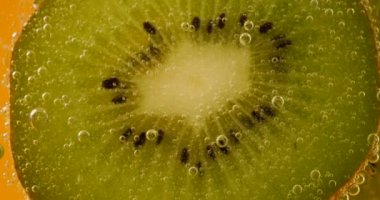 Ripe kiwi slices in air bubbles on an orange background.