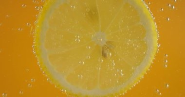 A slice of ripe lemon in water bubbles on an orange background.