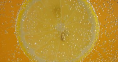 A slice of ripe lemon in air bubbles on an orange background.