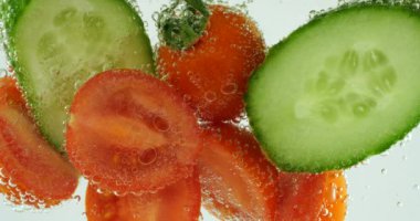 Slices of fresh cucumbers and tomatoes in clear water in air bubbles.