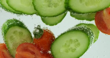 Slices of fresh cucumbers and tomatoes in clear water in air bubbles.