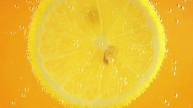 A slice of ripe lemon in water bubbles on an orange background.