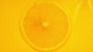 A slice of orange is filled with water with air bubbles on an orange background.