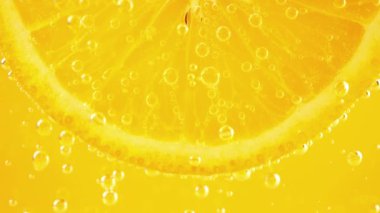 A slice of ripe orange in water bubbles on an orange background.