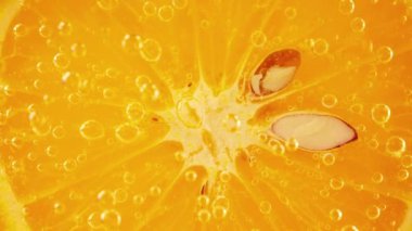 A slice of ripe orange in water bubbles on an orange background.