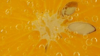 A slice of ripe orange in water bubbles on an orange background.