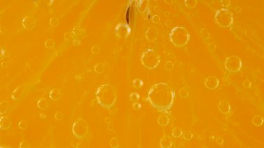 A slice of ripe orange in water bubbles on an orange background.