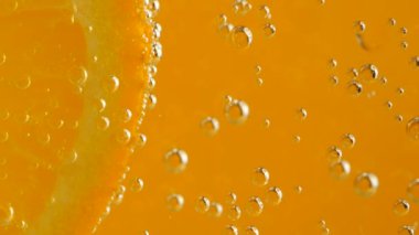A slice of ripe orange in water bubbles on an orange background.