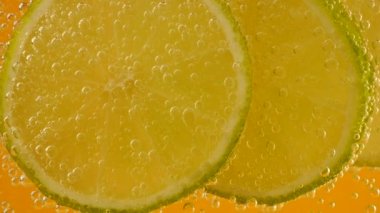 Ripe lime slices in air bubbles on an orange background.