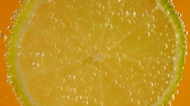 Turuncu arka planda, hava kabarcıklarında olgun bir limon dilimi..