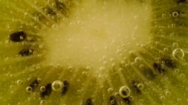 Ripe kiwi slices in air bubbles on an orange background.