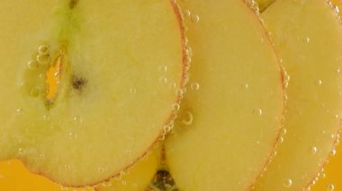 Ripe apple slices in air bubbles on an orange background.