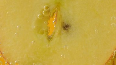 Ripe apple slices in air bubbles on an orange background.