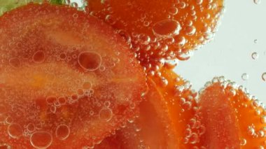 Slices of fresh cucumbers and tomatoes in clear water in air bubbles.