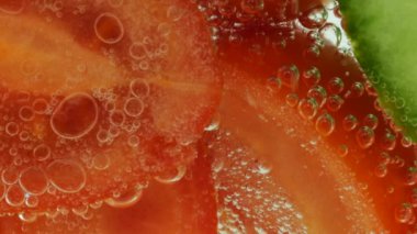 Slices of fresh cucumbers and tomatoes in clear water in air bubbles.