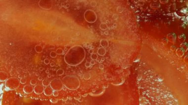 Slices of fresh cucumbers and tomatoes in clear water in air bubbles.