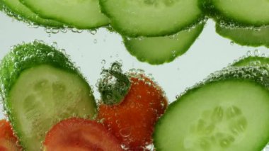 Slices of fresh cucumbers and tomatoes in clear water in air bubbles.