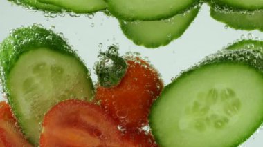 Slices of fresh cucumbers and tomatoes in clear water in air bubbles.