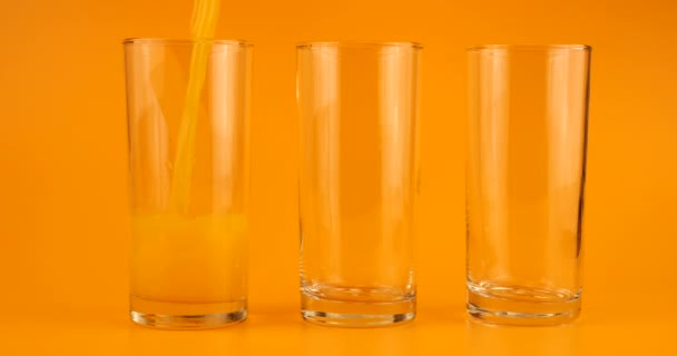 Sok Pomarańczowy Wlewa Się Szklanych Pucharów Pomarańczowym Tle Zwolniony Ruch — Wideo stockowe