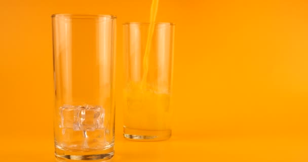 Апельсиновый Сок Наливают Стеклянные Чашки Льдом Оранжевом Фоне Медленное Движение — стоковое видео