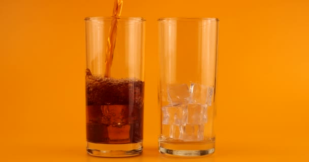 オレンジ色の背景に氷を入れたガラスのゴブレットにコーラを注ぐ スローモーション — ストック動画