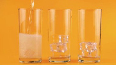 Karbonatlı limonata, turuncu arka planda buzlu cam kadehlere dökülür. Yavaş çekim.