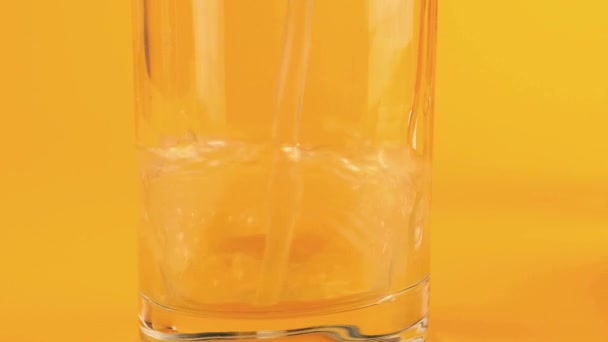 オレンジの背景にガラスのゴブレットにアップルジュースを注ぎます スローモーション — ストック動画