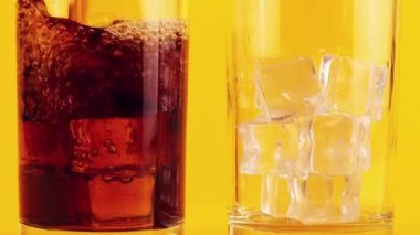 Kola, sarı zemin üzerinde buz bulunan cam kadehlere dökülür. Yavaş çekim.