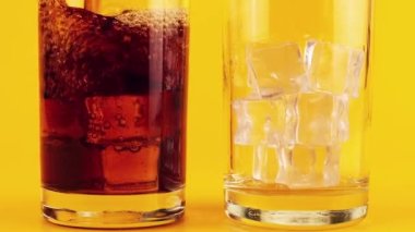 Kola, sarı zemin üzerinde buz bulunan cam kadehlere dökülür. Yavaş çekim.