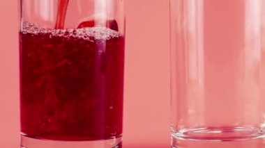 Nar suyu pembe arka planda cam kadehlere dökülür. Yavaş çekim.