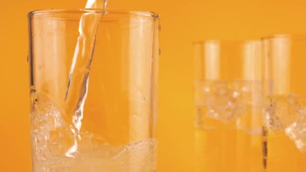 炭酸レモネードはオレンジ色の背景に氷を入れたガラスのゴブレットに注ぐ スローモーション — ストック動画