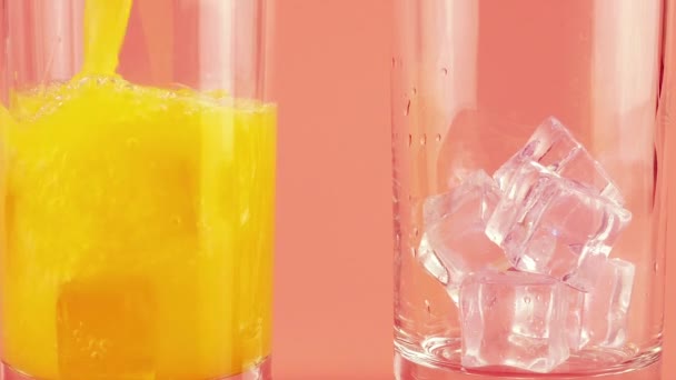 Sinaasappelsap Wordt Gegoten Glazen Bekers Met Ijs Een Roze Achtergrond — Stockvideo
