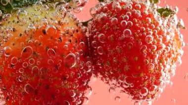 Pembe arka planda, hava kabarcıklarında olgun çilekler..