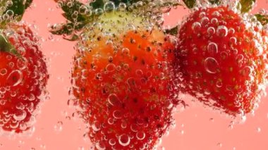 Pembe arka planda, hava kabarcıklarında olgun çilekler..