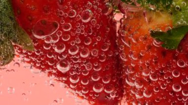 Pembe arka planda, hava kabarcıklarında olgun çilekler..