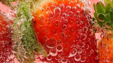 Pembe arka planda, hava kabarcıklarında olgun çilekler..