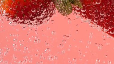 Pembe arka planda, hava kabarcıklarında olgun çilekler..