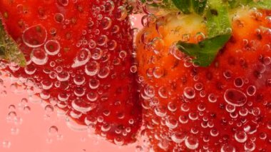 Pembe arka planda, hava kabarcıklarında olgun çilekler..