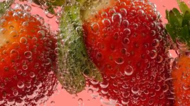 Pembe arka planda, hava kabarcıklarında olgun çilekler..