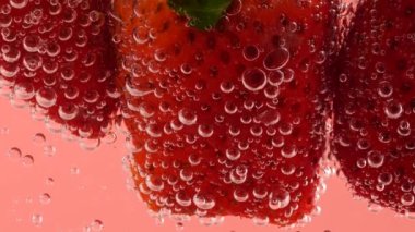 Pembe arka planda, hava kabarcıklarında olgun çilekler..