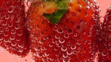 Pembe arka planda, hava kabarcıklarında olgun çilekler..