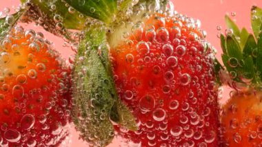 Pembe arka planda, hava kabarcıklarında olgun çilekler..